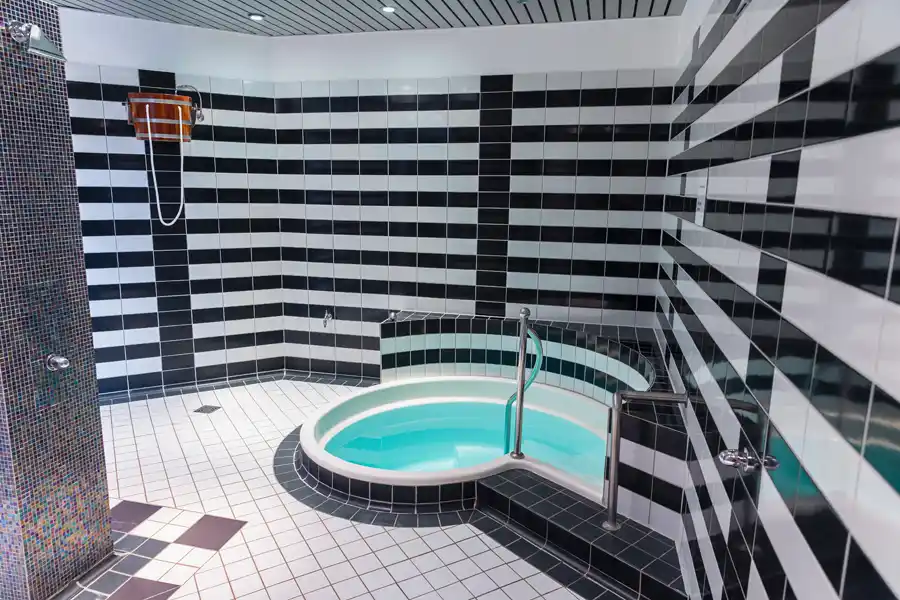 Kleines rundes Tauchbecken in schwarz-weiß gefliestem Raum mit Haltegriff und kühlem Wasser.