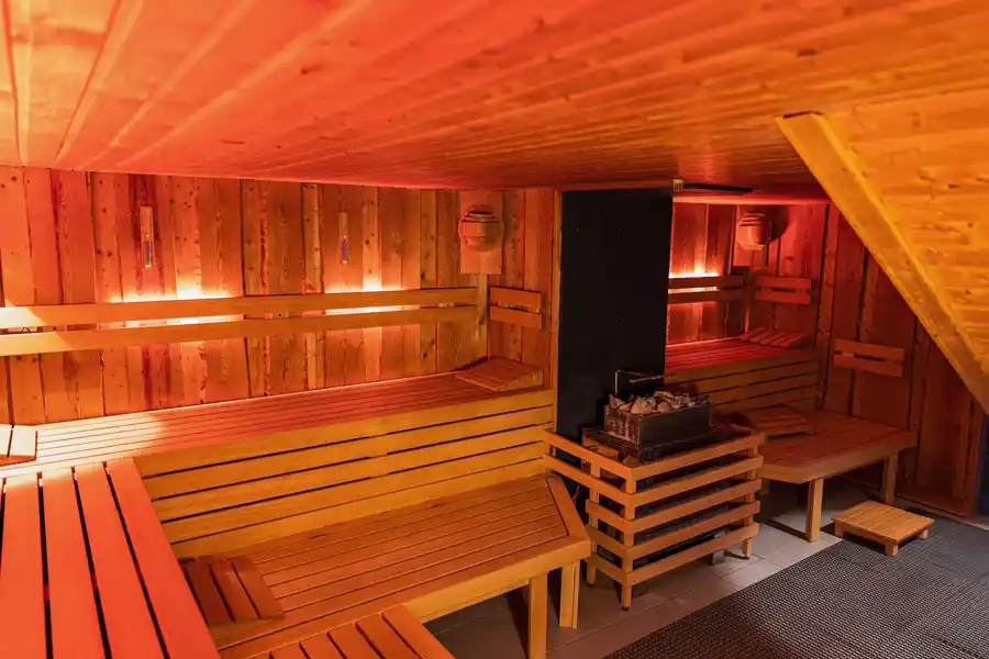 Finnische Sauna Innenansicht einer klassischen Finnischen Sauna aus hellem Holz mit Bänken und Ofen in gemütlicher Atmosphäre.