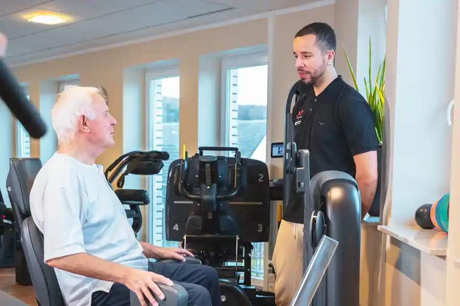 Therapeut begleitet Patient beim Krafttraining am Gerät.