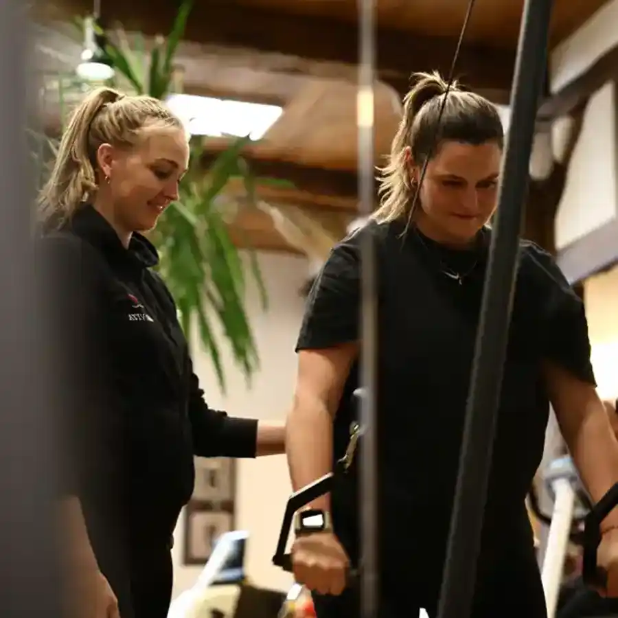 Begleitetes Krafttraining Trainerin unterstützt eine Frau beim Krafttraining an einem Seilzuggerät in der medizinischen Trainingsfläche.
