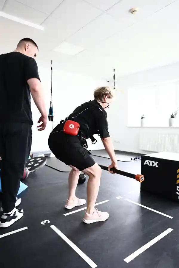 EMS-Training mit einer Langhantel Trainer begleitet eine Frau beim EMS-Training mit Langhantel.
