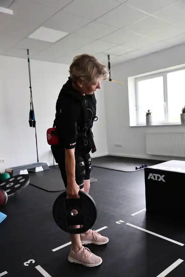 Langhanteltraining mit EMS-Unterstützung. Frau hebt in EMS-Anzug eine Langhantel mit beidseitiger Führung.