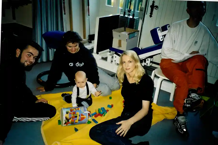 Erste Eindrücke:Familiäre Atmosphäre bei AKTIVITA Historisches Foto aus den Anfängen von AKTIVITA: Erwachsene und Baby auf Spieldecke in familiärer Therapiesituation