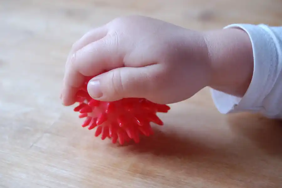 ensorik-Training in der Kinderphysiotherapie. Kinderhand hält einen roten Igelball – sensorisches Training zur Förderung der Motorik und Wahrnehmung in der Kindertherapie.