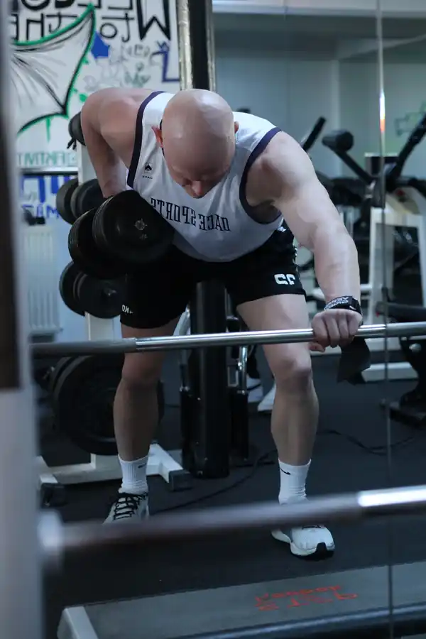 Athlet mit Kurzhanteln im B.E. GYM Athlet mit Muskelshirt mit Kurzhanteln macht intensives Krafttraining für Rücken und Bizeps.