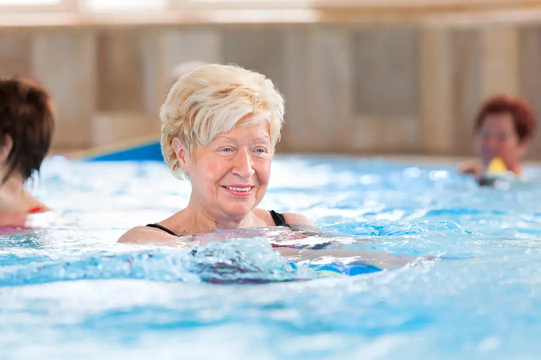 Schwimmkurs im AKTIVITA SoleSpa Ältere Frau lächelt beim Aquatraining im warmen Schwimmbad, umgeben von weiteren Teilnehmenden.